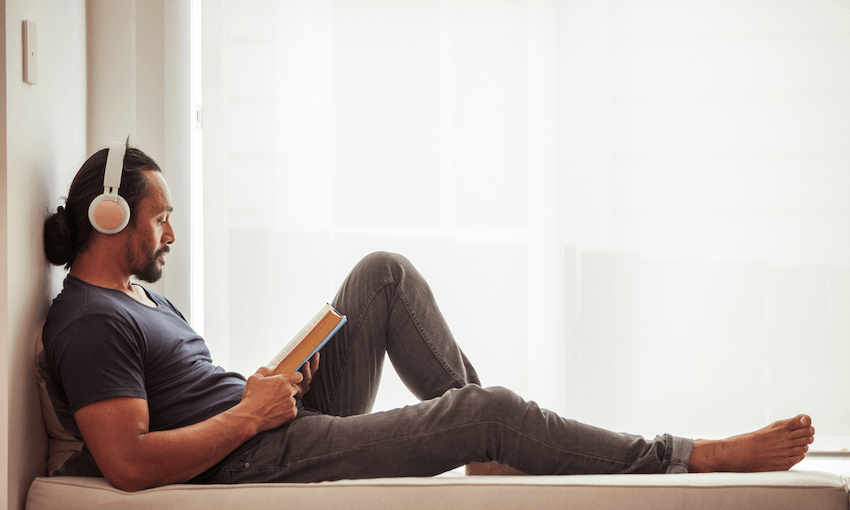 A man sits in a window seat, headphones on, reading