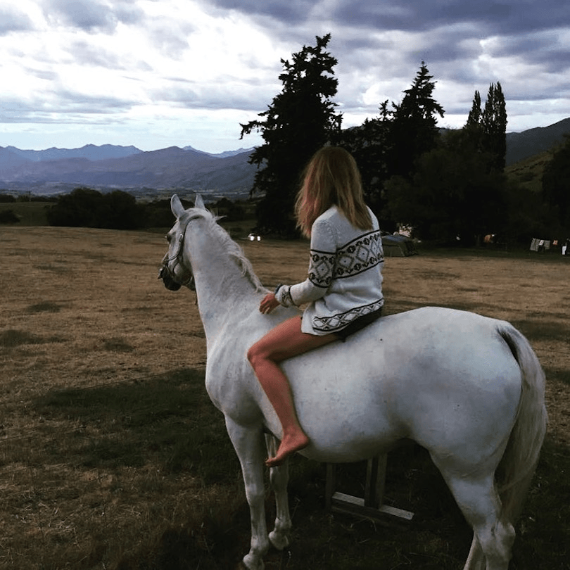 Woman on horse, facing away from camera, looking at mountain range in distance.