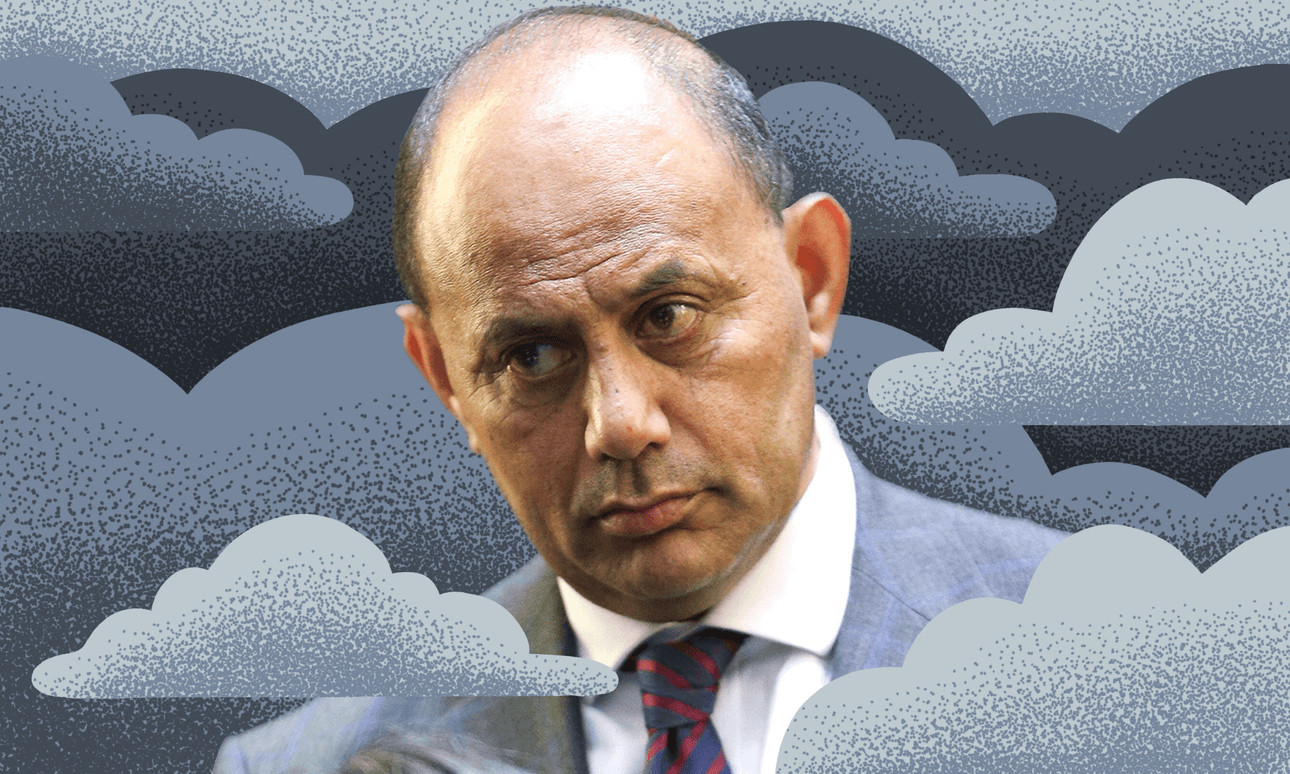 A man in a suit and striped tie is depicted against a background of illustrated gray clouds. He has a serious expression, with a bald head and some hair on the sides. The surreal backdrop contrasts with his realistic appearance.